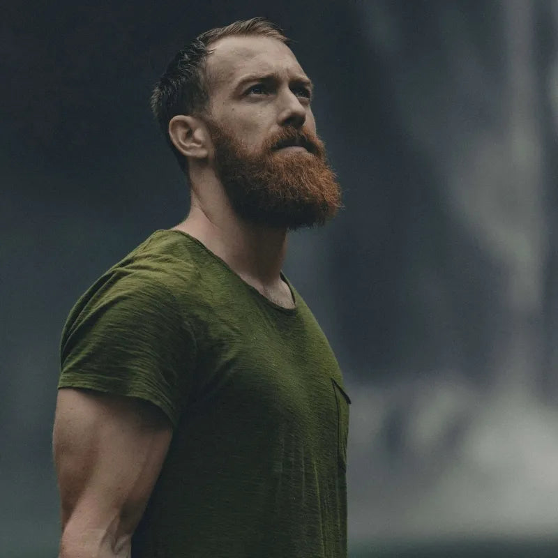 Man with a beard looking upwards, wearing a green shirt in a misty environment.